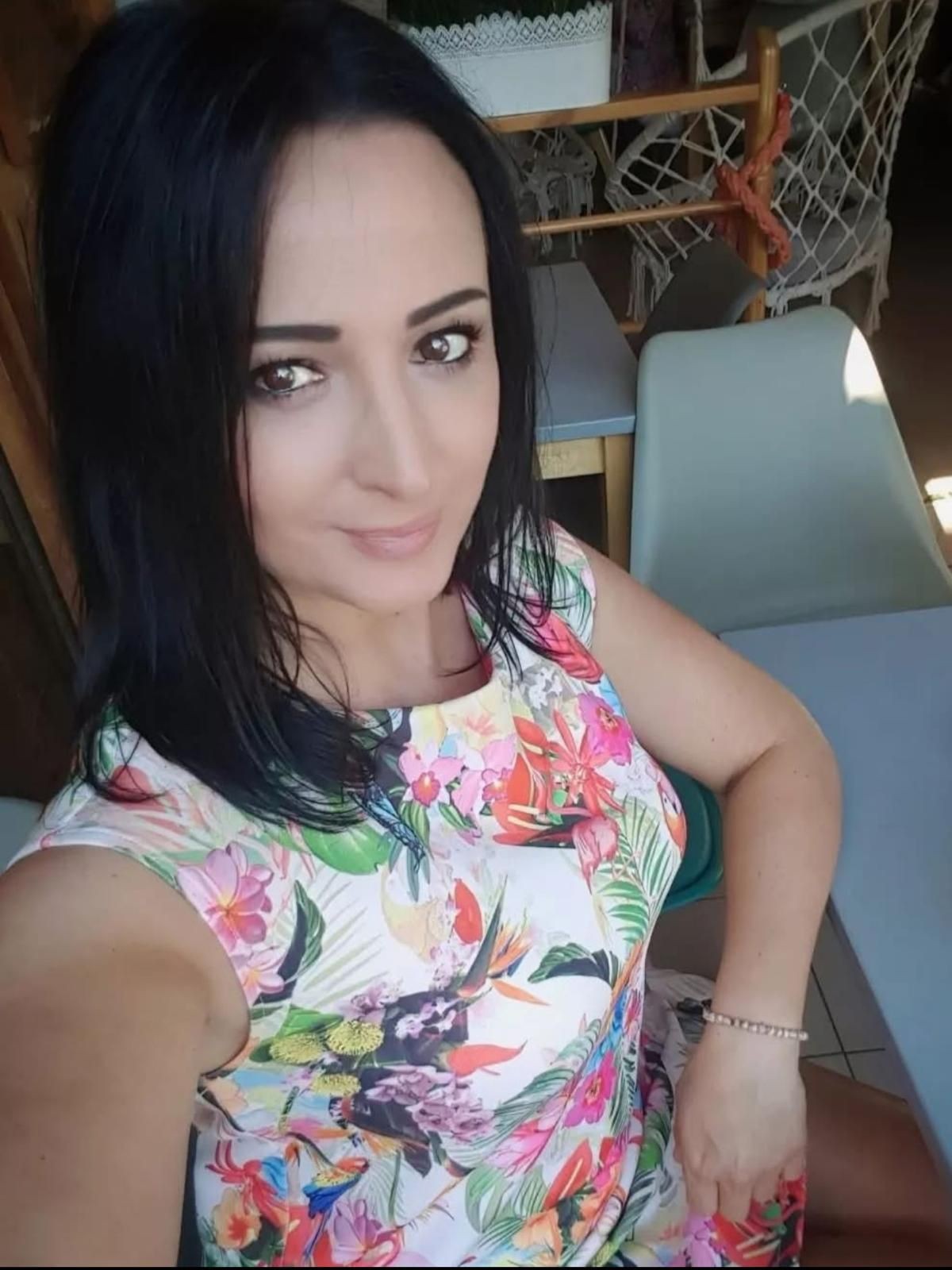 Woman taking a selfie in a floral dress while sitting at a table.