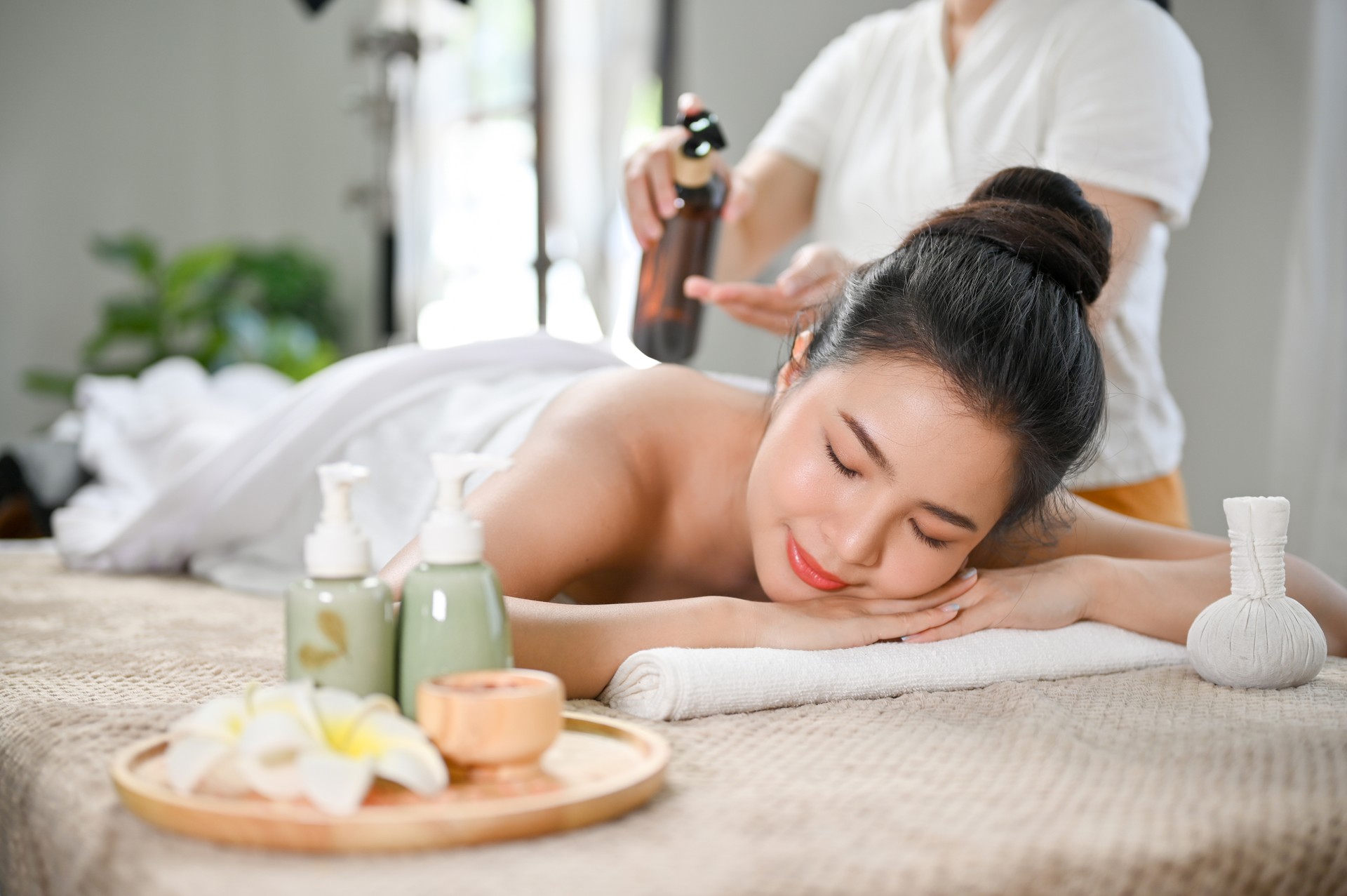 Relaxed Asian woman lying on massage table, receiving body massage, enjoying Thai spa at salon.